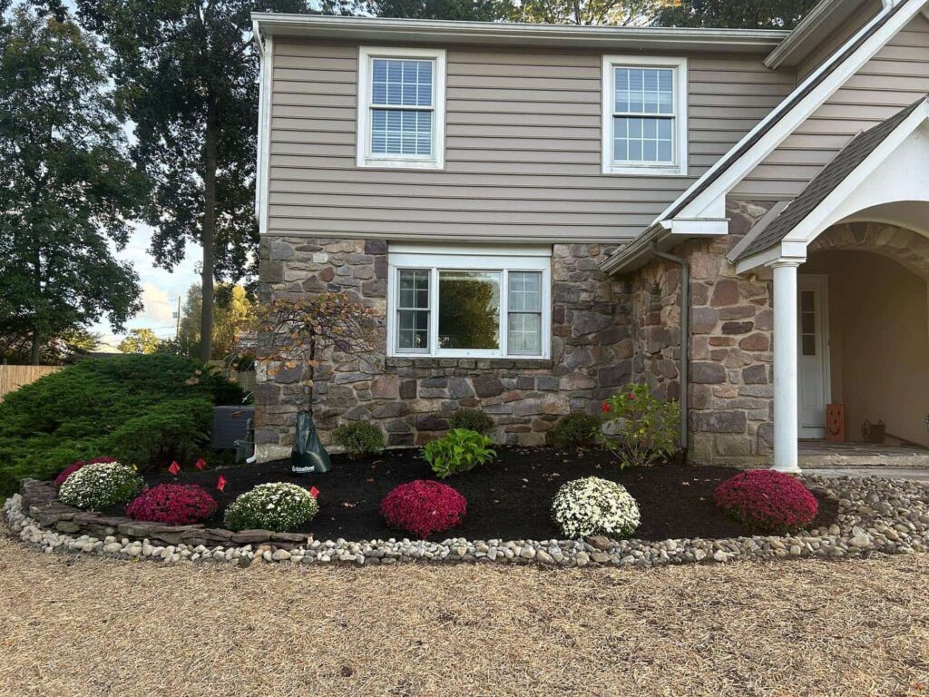Front yard landscape bed with fresh mulch, decorative stone border, flowering shrubs, and foundation plantings in front of a stone home