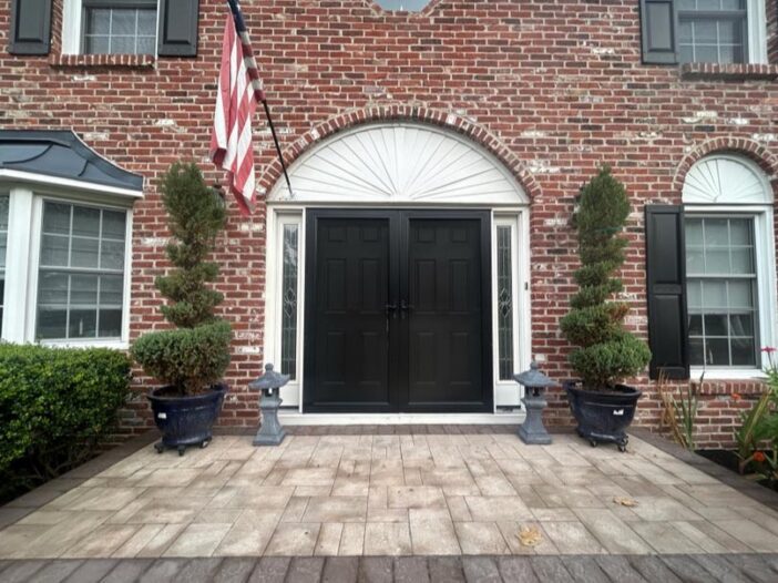 A brick front door adorned with a flag and two planters, highlighting stone masonry and a welcoming pathway.