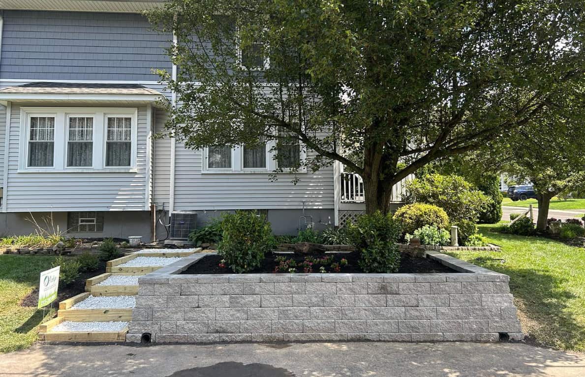 Raised landscape bed with retaining wall, gravel steps, fresh mulch, and shrubs in front of a residential home