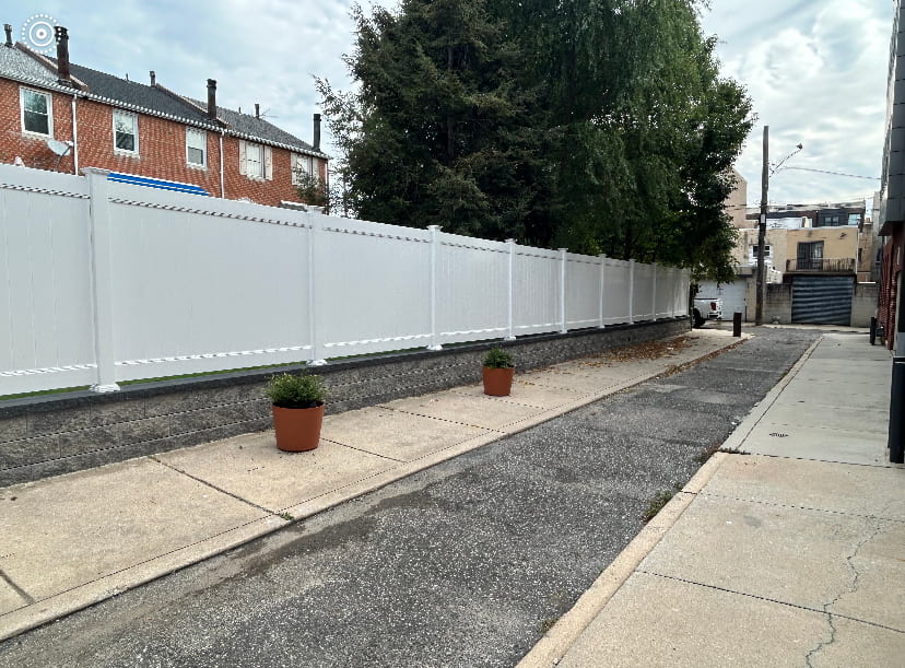 Long white vinyl privacy fence installed along a residential property line beside an alley and concrete walkway